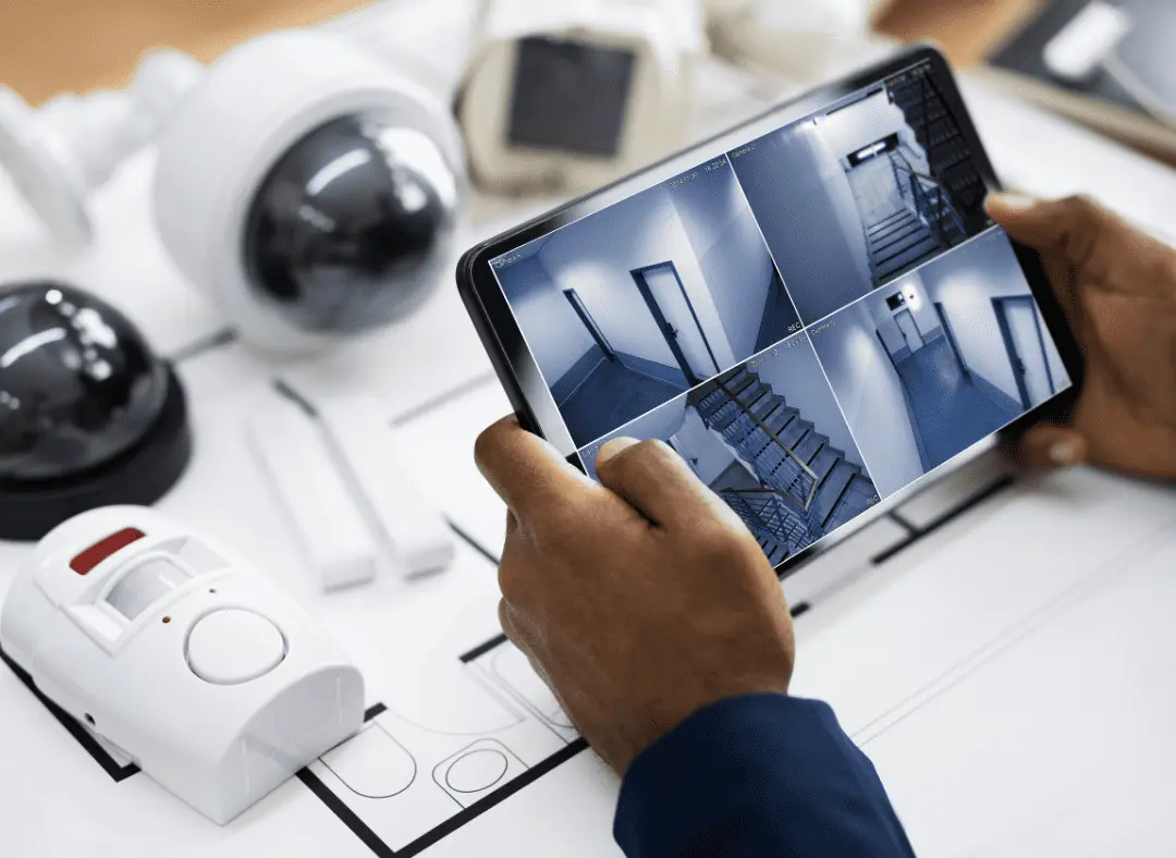 Person monitoring home security cameras on a tablet screen, showing live footage from multiple smart cameras.