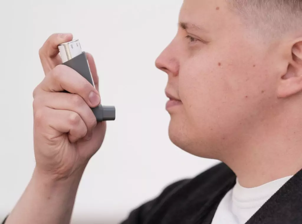 Man using an asthma inhaler for relief indoors, highlighting connection between air conditioning and asthma symptoms